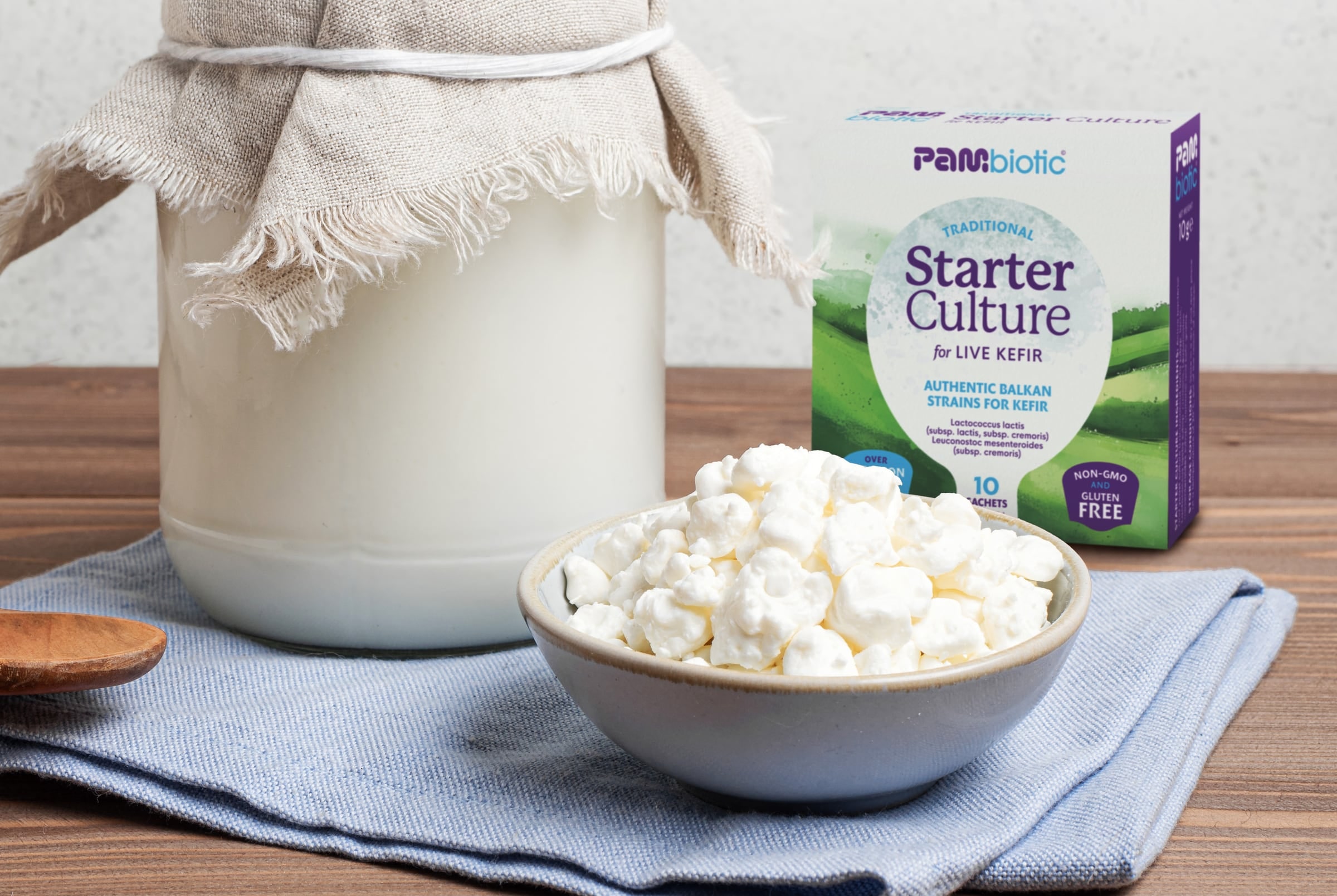 A jar of milk under linen and a bowl of kefir next to the Pambiotic kefir starter box