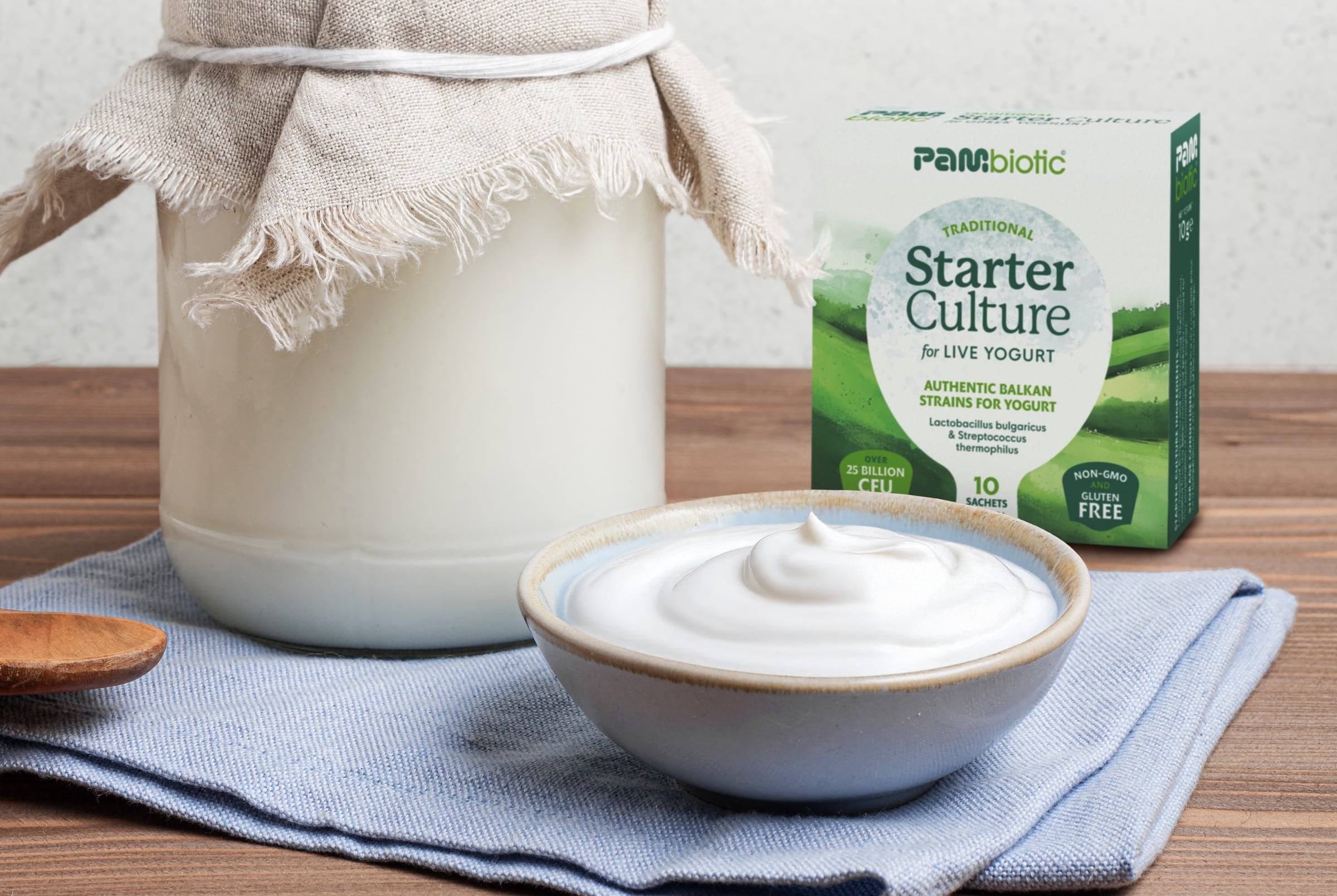 A jar of milk under linen, a bowl of homemade yogurt and the Pambiotic yogurt starter box